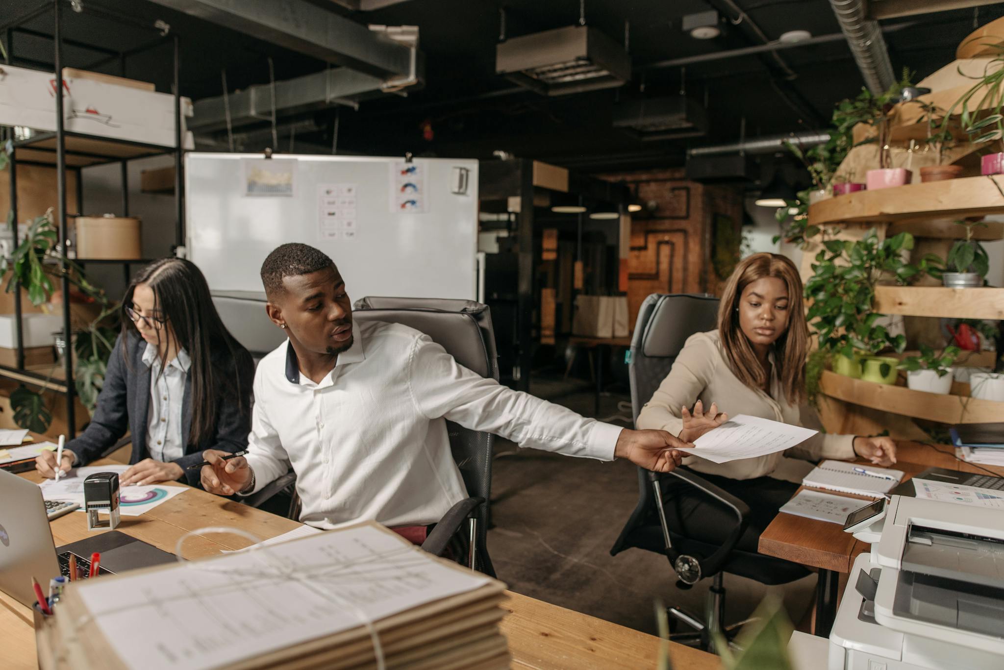 A group of colleagues working together in a modern, plant-filled office, discussing documents.
